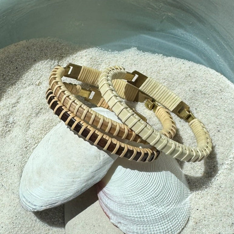 Handcrafted Nauti Clasp Bracelets in mahogany and holly variants with brass clasps, arranged on seashells in sand, made by military spouse artisans at Stonington Designs.