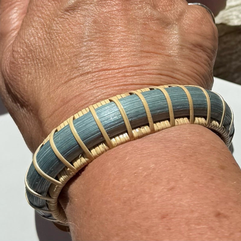 Harbor Mist statement cuff worn on the wrist, showing the hand-dyed blue bamboo weave and cherry end caps in natural light.