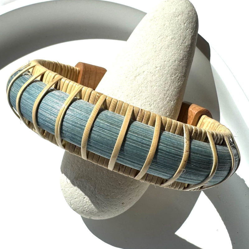 Harbor Mist cuff bracelet from the Marsh Collection, hand-dyed blue bamboo with cherry wood end caps, displayed on a natural stone.