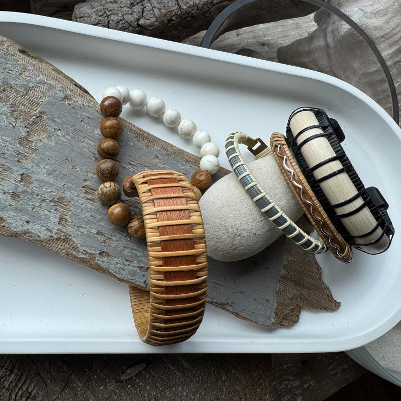 Moonbeam black and white cuff beside other wood and beaded bracelets in a styled tray.