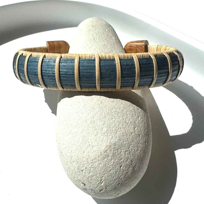 Tidewater cuff bracelet from the Marsh Collection, hand-dyed blue bamboo with hand-carved cherry end caps, displayed on a natural stone.