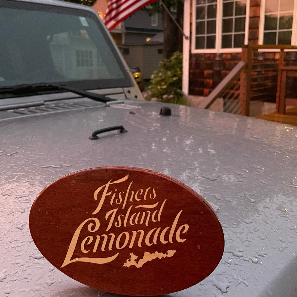 Fishers Island Lemonade inlay for a wooden hitch cover sitting on the hood of a car in front of a porch with US flag