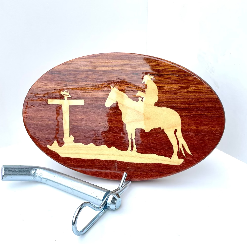 A wooden hitch cover featuring a cowboy and a horse in the center, with a maple inlay design around the edge.