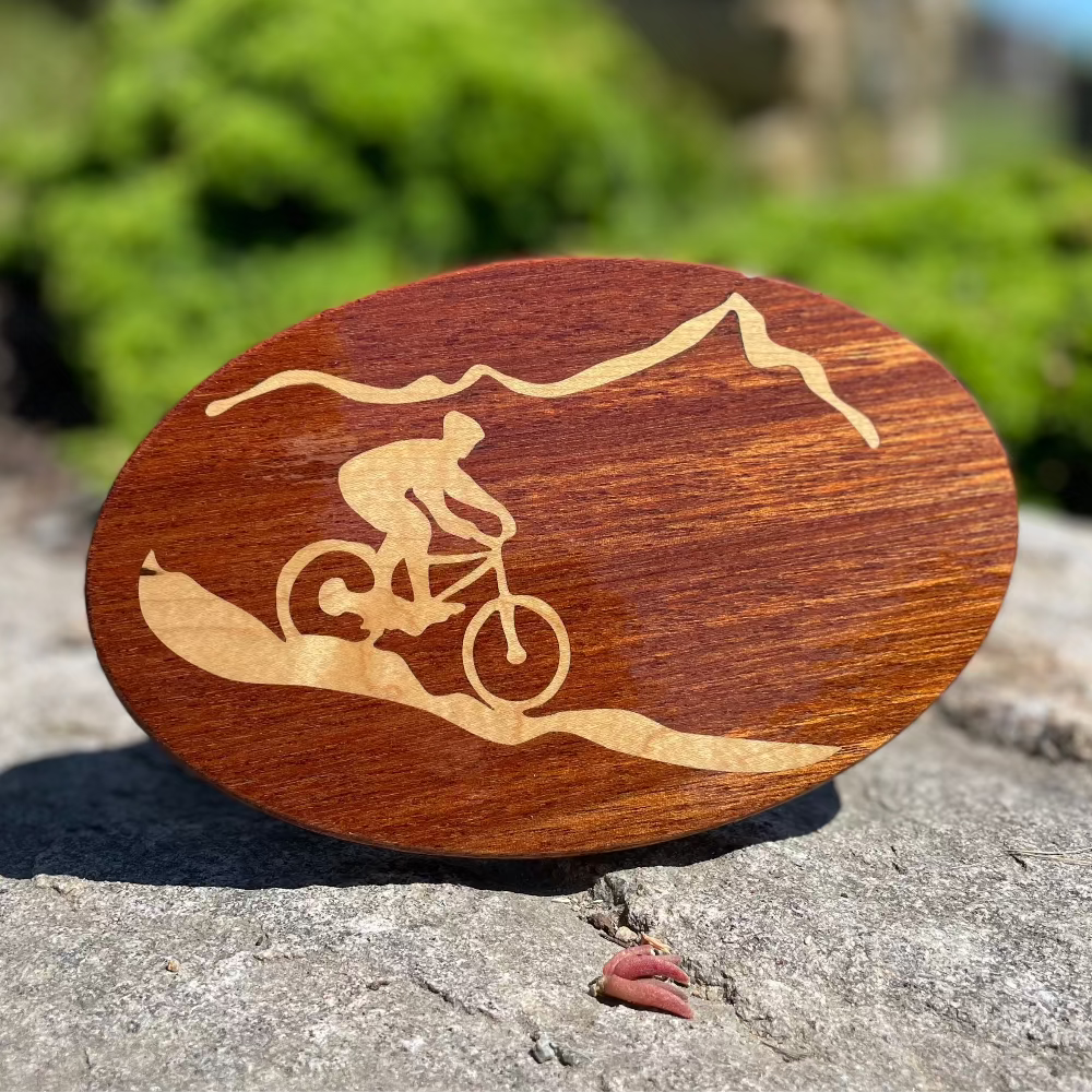 mountain biker on a path in front of a mountain - design on a wood hitch cover balanced on a rock