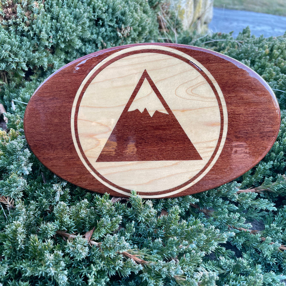 inlay mountain in circle on wooden hitch cover resting on a green bush