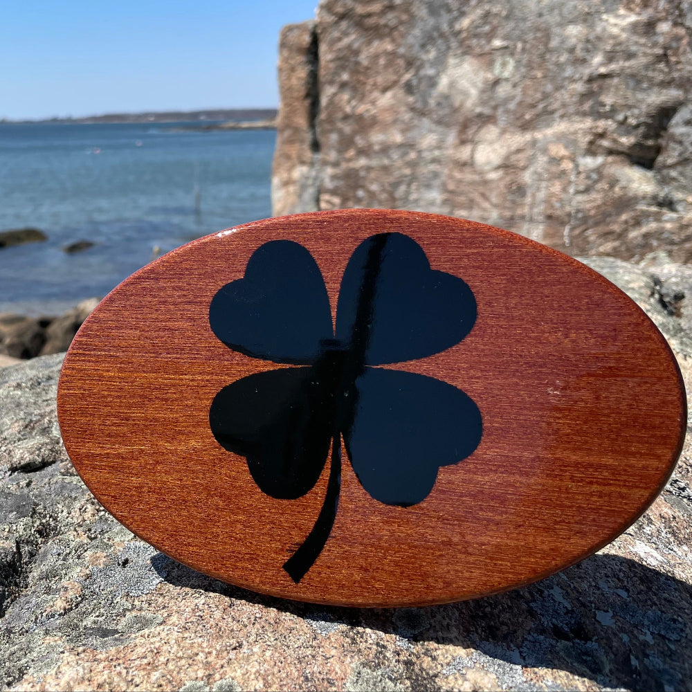wood inlay hhitch cover with black four-lead clover, on rock backgrouns iwth some water