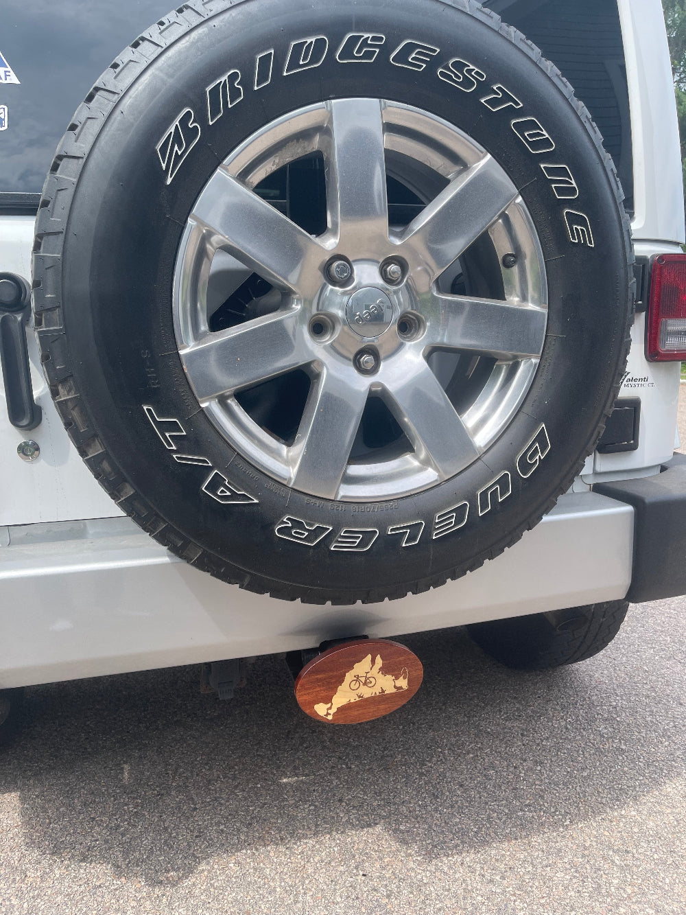 A wooden hitch cover with a maple inlay, designed with a bicycle and the outline of Martha's Vineyard in a hitch on the back of a Jeep 