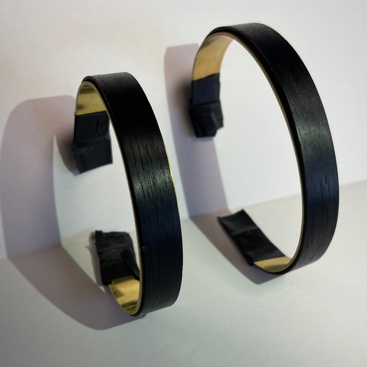 ebony wood staves around brass cuffs leaves vertically againt a wall to show 3 sizes