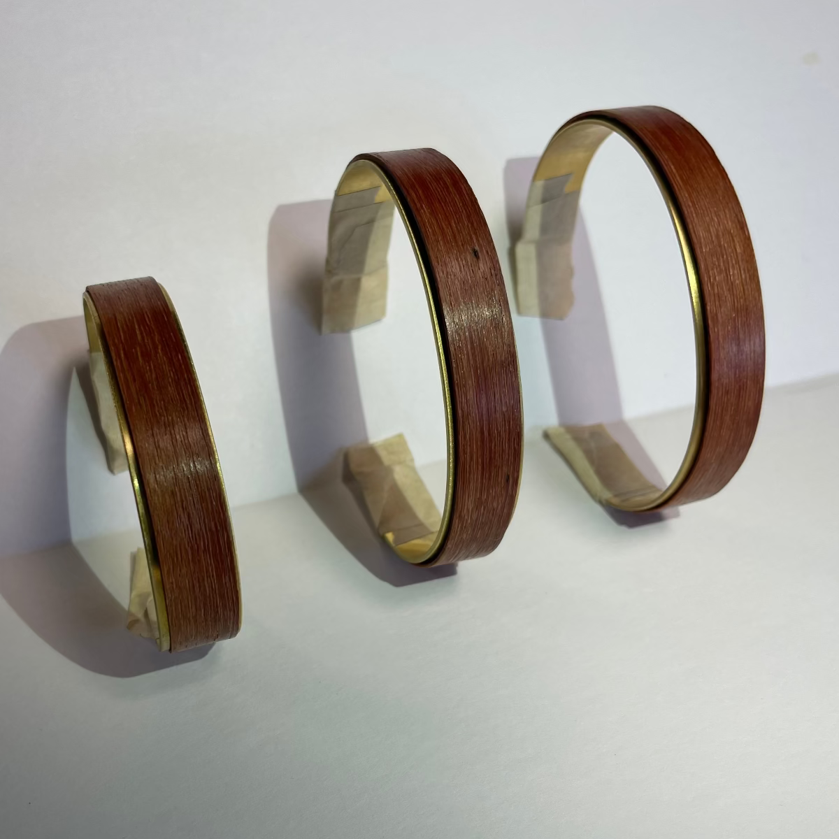 three brass cuffs with blank staves leaned against a wall vertically to show 3 sizes available