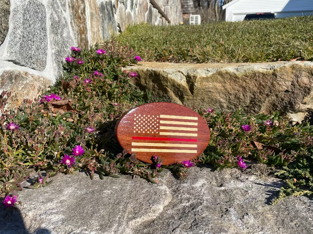 wood hitch cover with US flag and a thin red line as a stripe in the middle, balanced on a rock with greenery behind it
