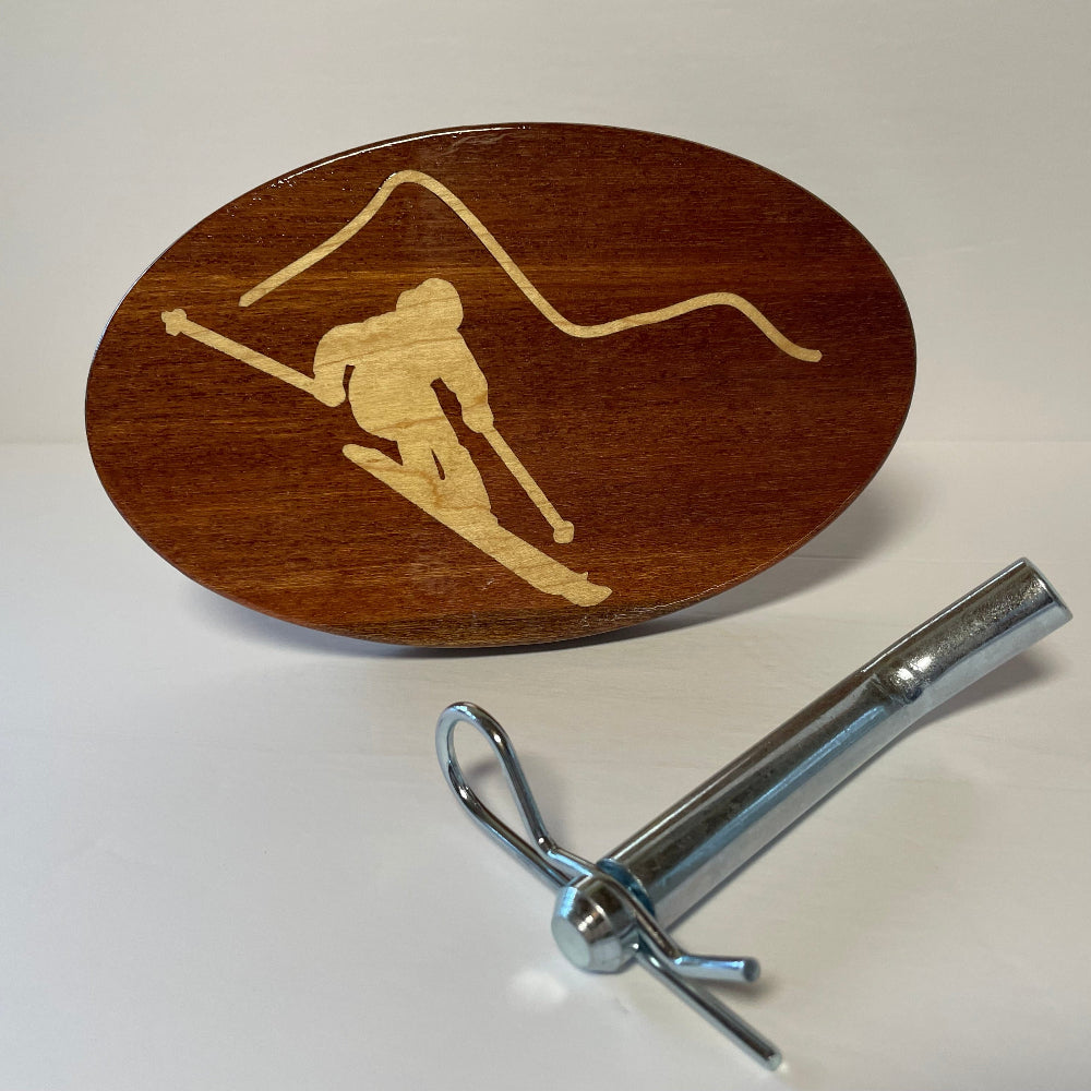 Solid mahogany hitch cover with a maple inlay design of a skier, accompanied by a metal hitch mount.