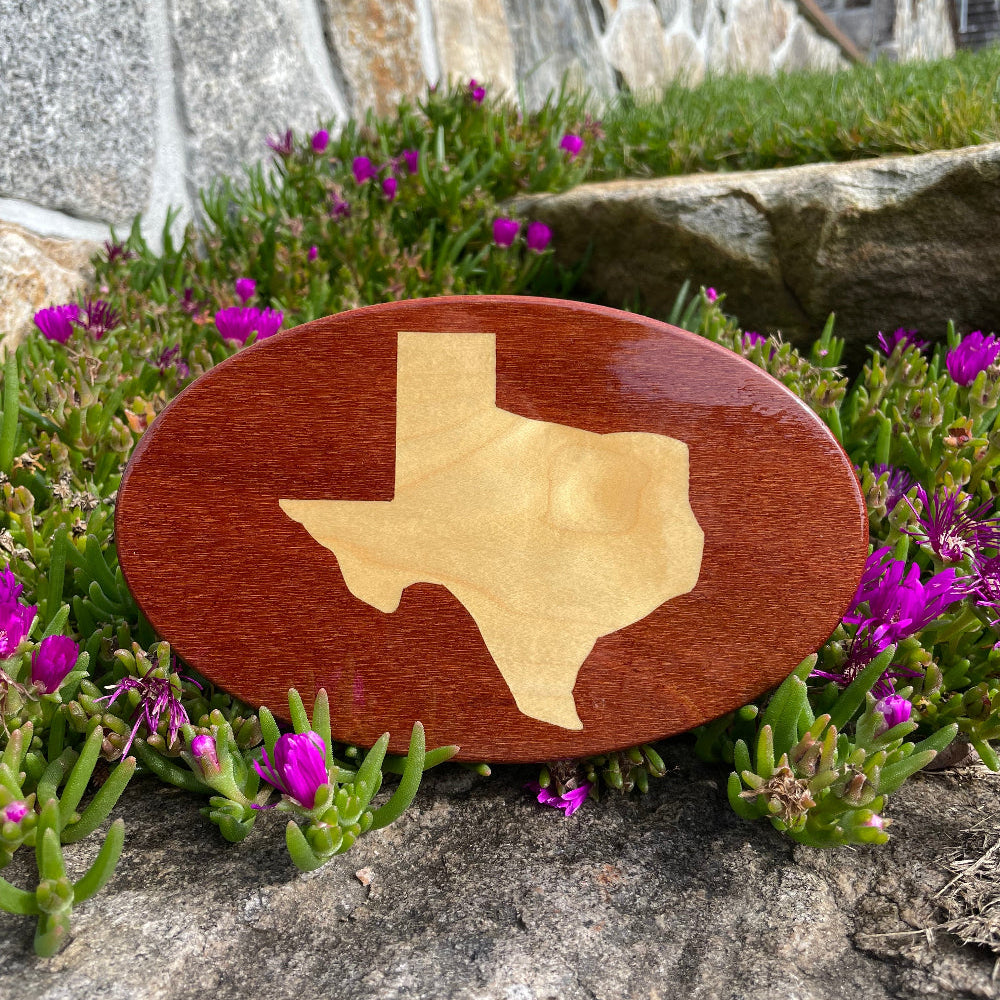 Texas state inlay on wooden hitch cover on rock in front of flowers